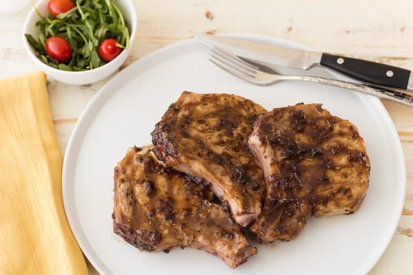 Three Pork Chops on a white plate with Raspberry Glaze and a side salad