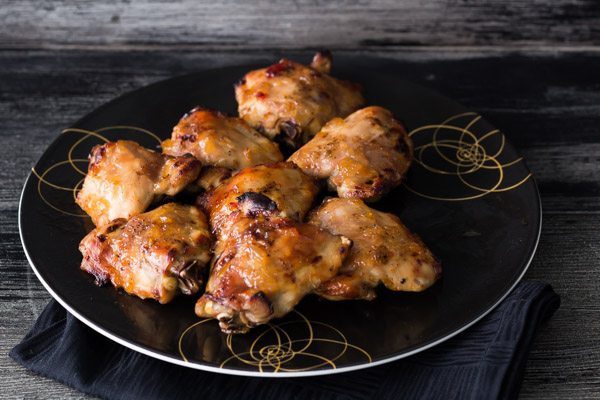 Eight Oven-Roasted Chicken Thighs on a round black plate seating on a black napkin. Quick and easy recipe with Roasted Pineapple Habanero Sauce. Spoonabilities.com