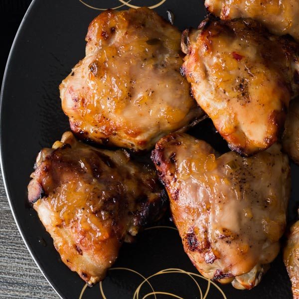 Six pieces of Oven-roasted Chicken Thighs with Roasted Pineapple Habanero Sauce on a black plate. Spoonabilities.com