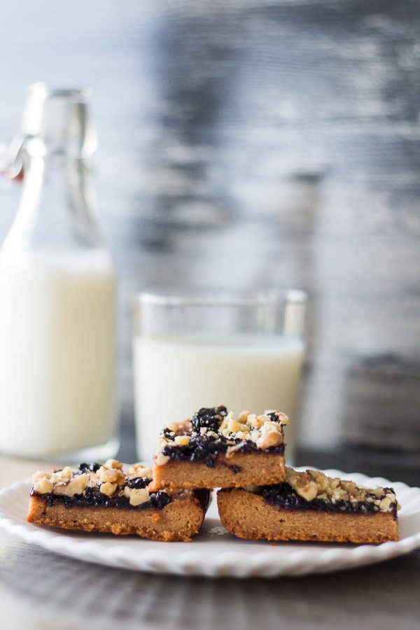 Three Peanut Butter Jelly Bars on a white plate in front of a glass and bottle of milk.