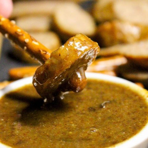 Pulling pretzel stick with a sausage bite out of a bowl of fig mustard