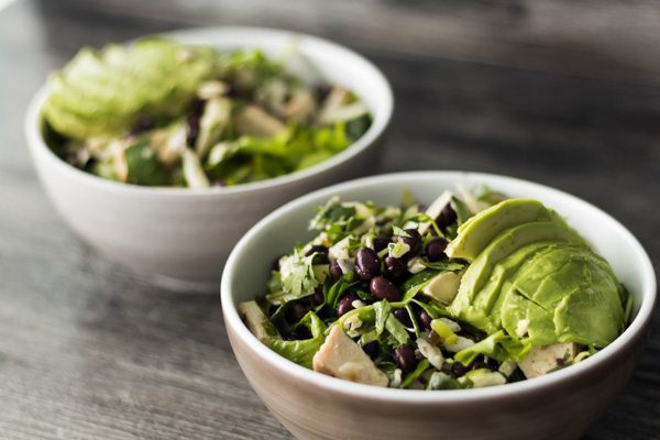 Two white bowls of summer salad full of avocado, black beans, chicken, cilantro and manchego cheese.