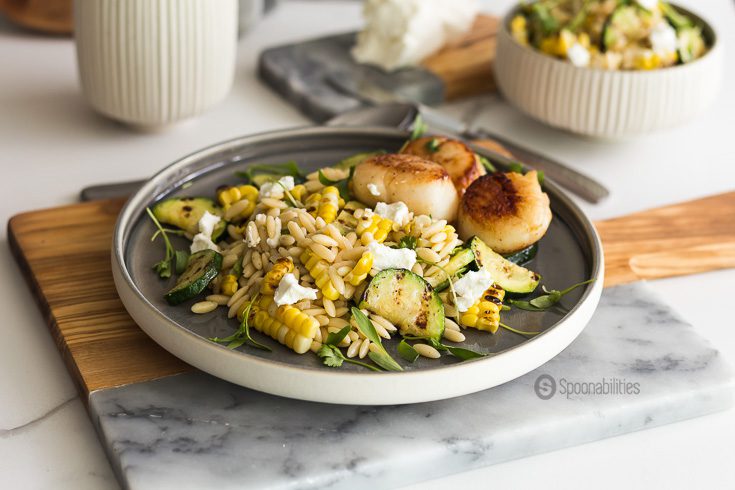 Grilled Corn Zucchini Orzo Salad with a perfect buttery seared scallop, topped with a tangy goat cheese and fresh cilantro micro greens. Spoonabilities.com