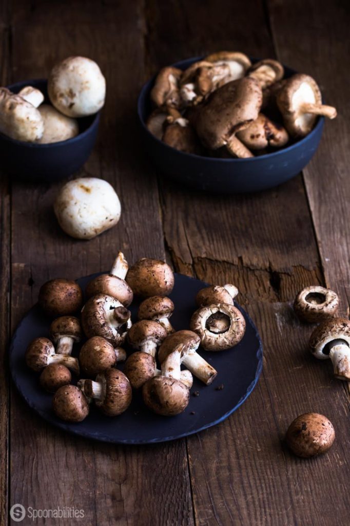 Three types of mushrooms in blue bowls on a wooden table