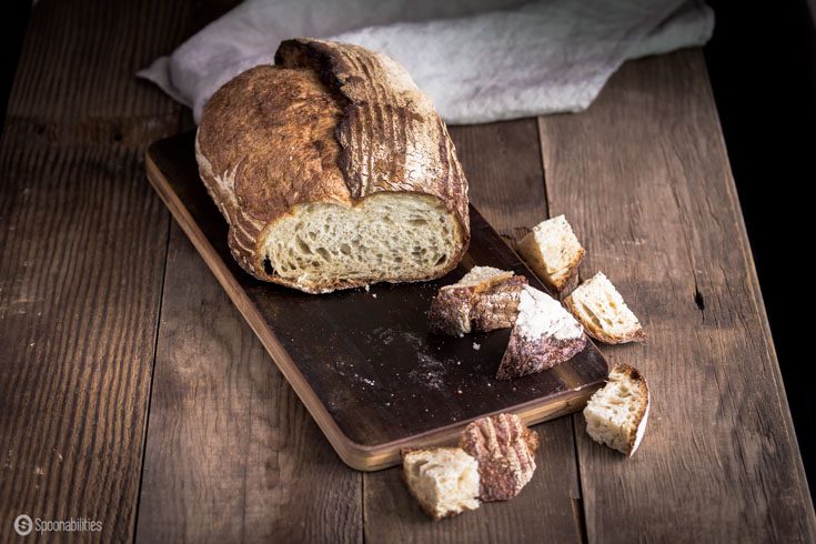 Loaf of sourdough bread on a dark wood table, with a few bread cubes cut off. Spoonabilities.com