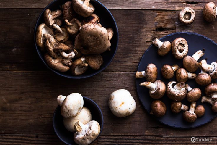 Three types of mushrooms in blue bowls on a wooden table