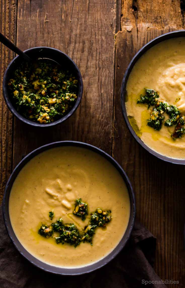 Two Black soup bowls with Creamy Celery Root Soup. This soup has celery root, leek, parmesan & Walnut-Parsley Gremolata. Spoonabilities.com