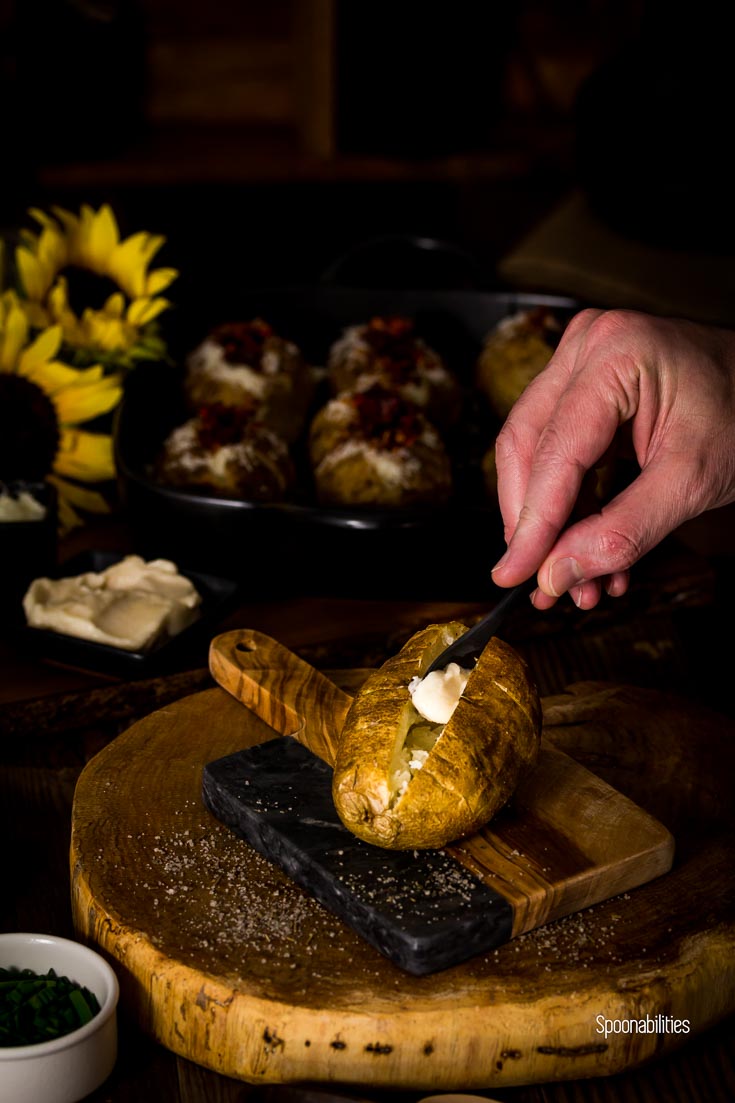 Adding a Tablespoon of aioli to the baked Spanish style baked potato, on a rustic cutting board. Spoonabilities.com