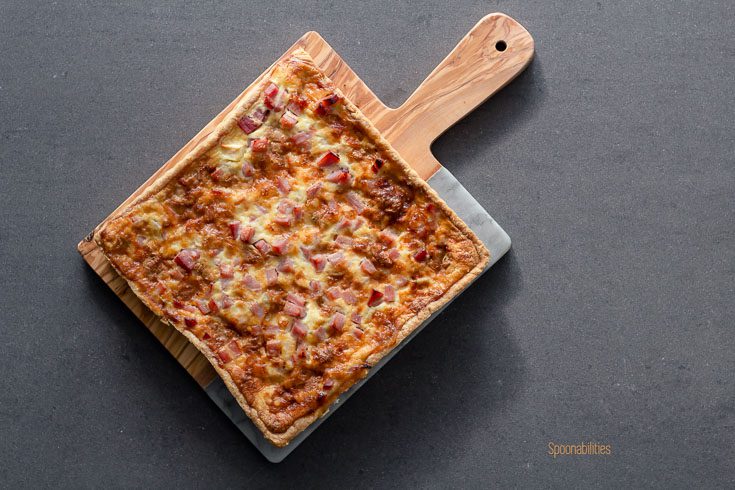 Square Époisses Ham Apple Tart displayed on a half wood half marble cutting board on a gray background. This tart is rich and excellent as an appetizer, dinner or party bites. Spoonabilities.com