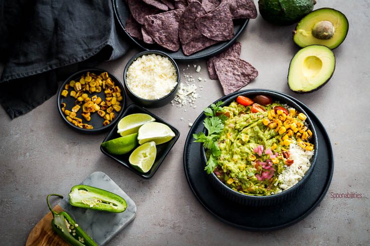 The best guacamole recipe presented in a black round bowl and served with blue corn tortillas and more Cinco de mayo recipes from Spoonabilities.com