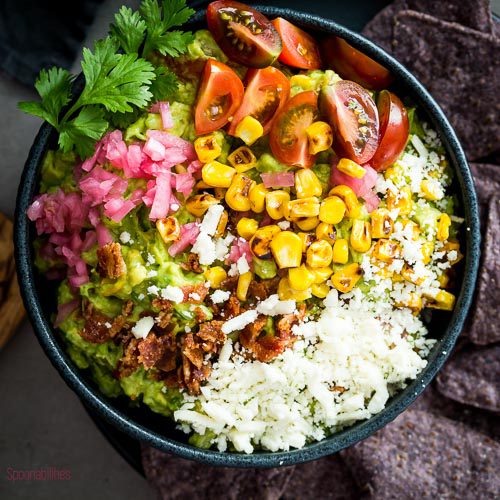 Plate of guacamole charred corn with bacon bits is the perfect cinco de mayo food to offer guests