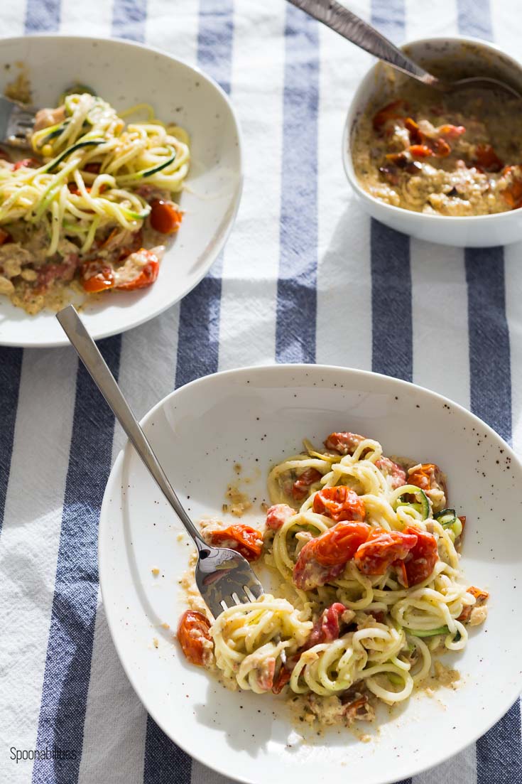 two plates with Zoodle (zucchini noodle) recipe inspired by Mediterranean flavors of lemon artichoke pesto, asiago cheese and roasted cherry tomatoes. Spoonabilities.com