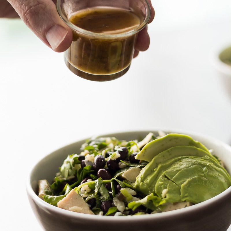 Jalapeno Raspberry Vinaigrette Dressing about to pour on a Mixed Green Salad with Chicken, Avocado, Black Beans, Cilantro, Green onions & Manchego Cheese. Spoonabilities