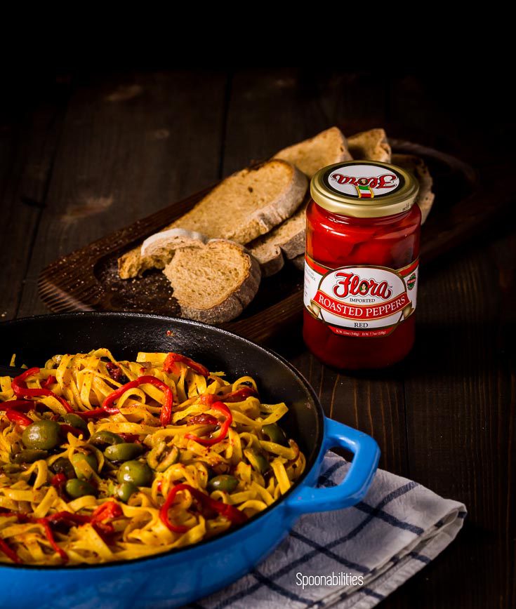 Blue skillet with Roasted Red pepper pasta next to a jar of roasted red pepper by Flora fine Foods. Spoonabilities.com