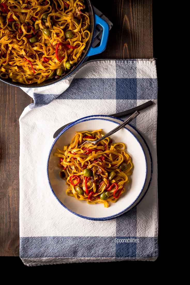 Overhead shot showing the table set up with a bowl of roasted red pepper pasta on a white & blue napkin and the skillet with pasta. Spoonabilities.com