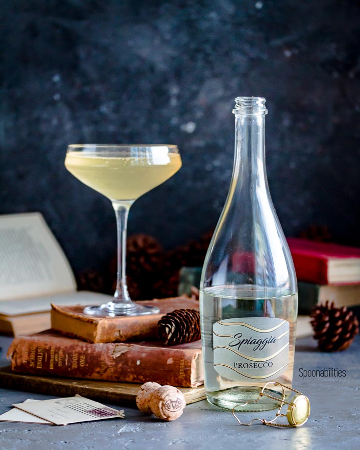 Gin Prosecco Cocktail in a coupe glass on top of antique books. Next to a bottle of Spiaggia Prosecco. Spoonabilities.com