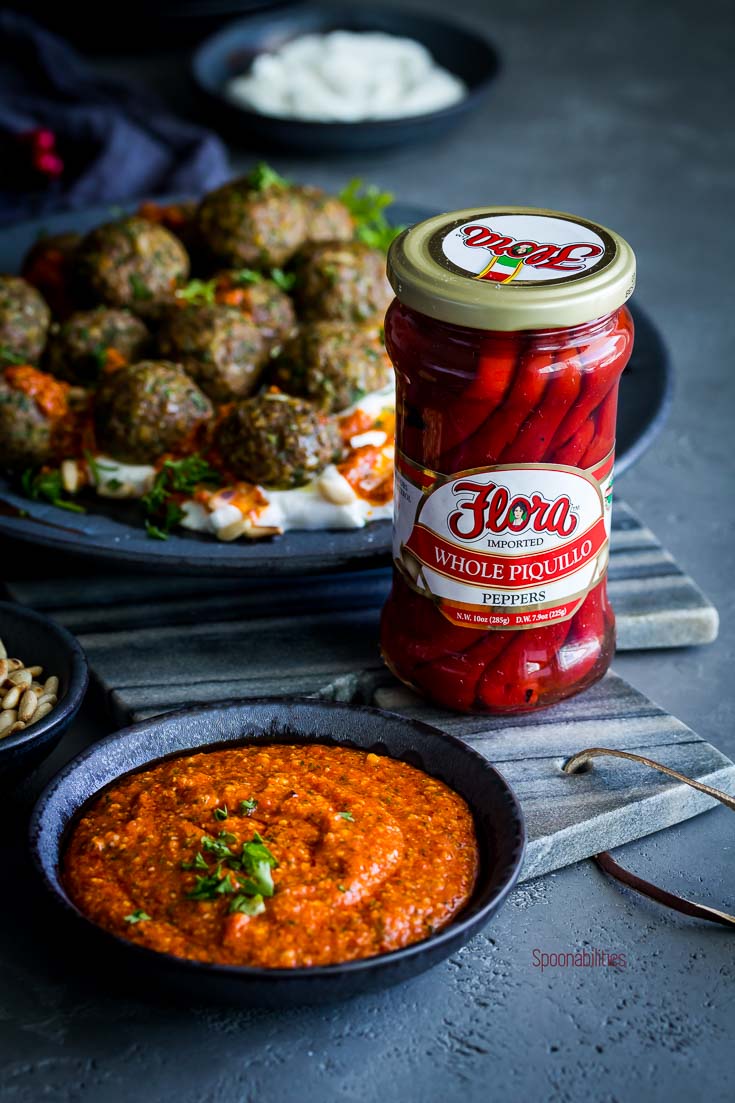 A jar of whole piquillo peppers from Flora Fine Foods on a marble tray . Next to a small bowl with piquillo pepper pesto. Spoonabilities.com