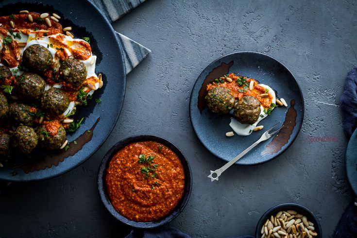 Large plate with Spiced Lamb Meatballs with two small bowls with piquillo pepper pesto, pine nuts and one small plate with two lamb meatballs. Spoonabilities.com