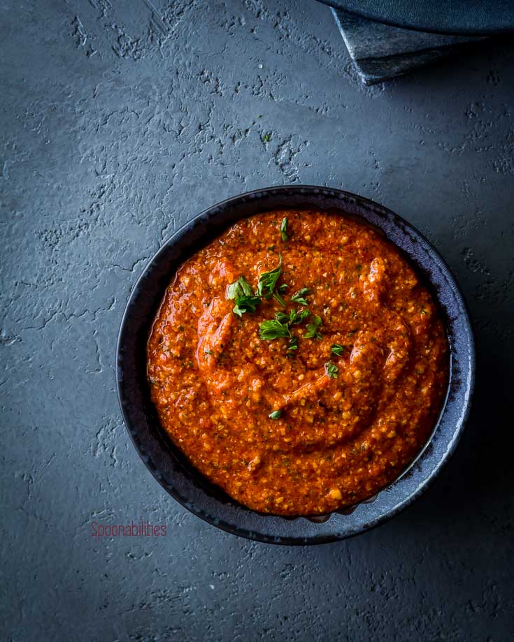 Piquillo pepper pesto in a small stone color bowl. Garnished with fresh chopped parsley. Spoonabilities.com