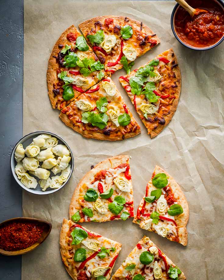 Two Cauliflower Crust Pizza cut into slices with Baby Artichokes and Roasted Red Pepper displayed in a parchment paper. Spoonabilities.com