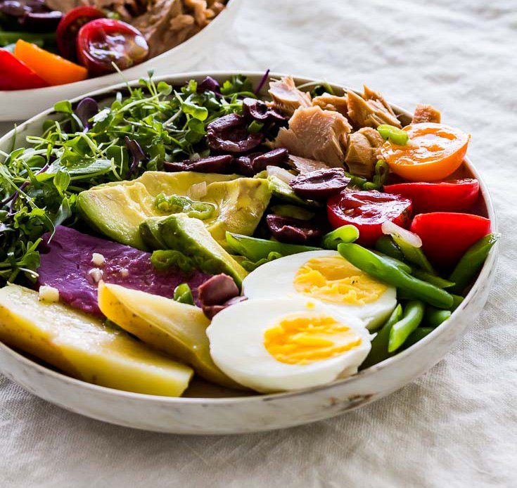 Large bowl of Nicoise Salad with Dijon mustard vinaigrette, on a gray tablecloth