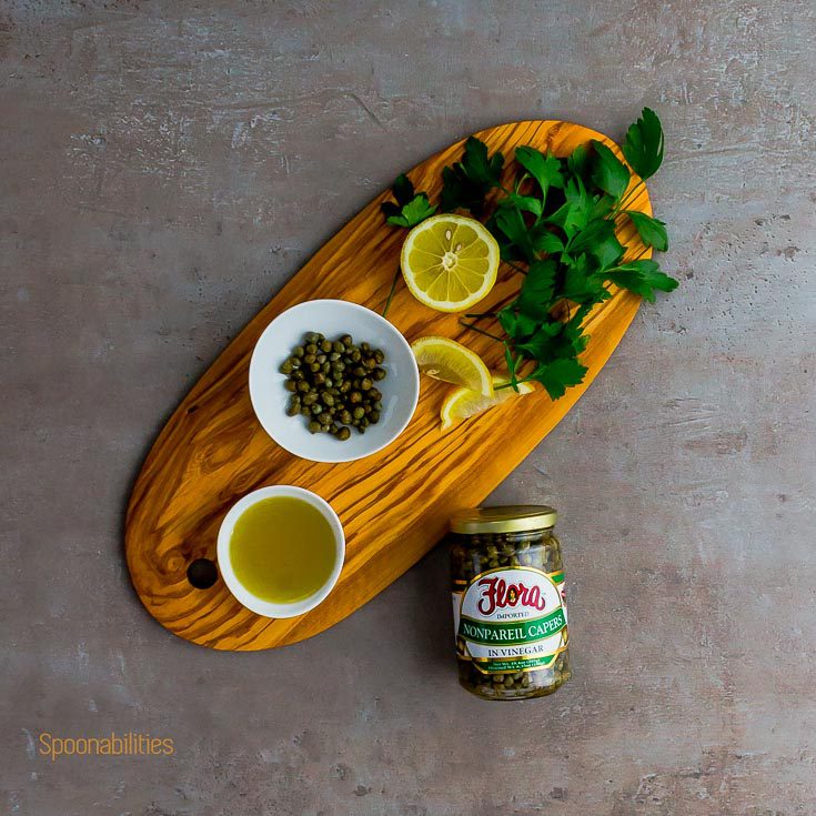 Wooden board with parsley, lemon, olive oil and Capers by Flora Fine Foods. Spoonabilities