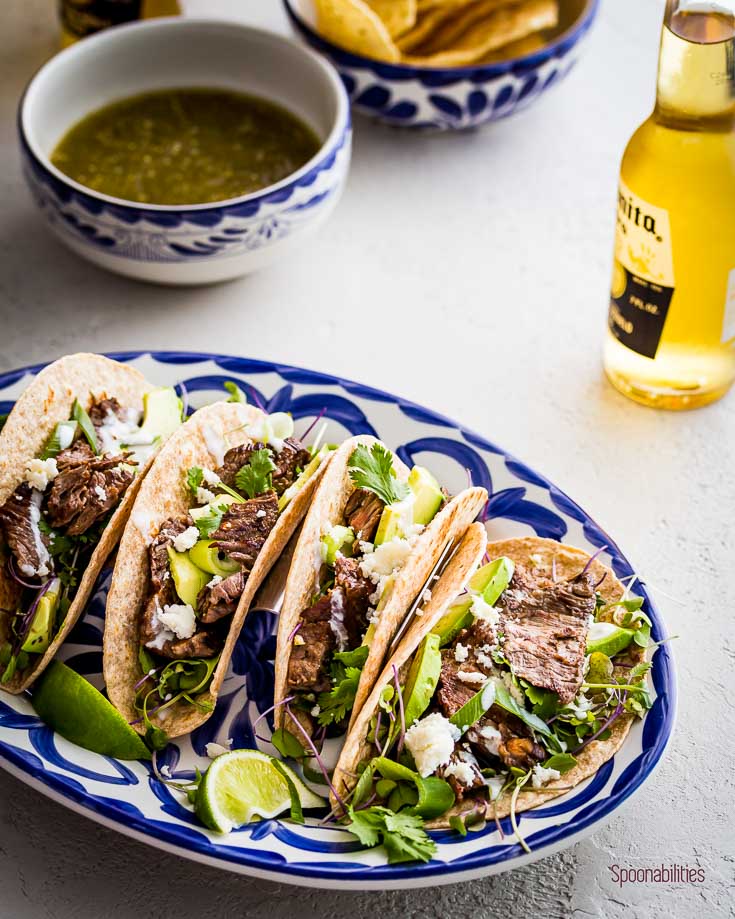 Juicy and tender grilled Skirt Steak Tacos on a oval serving plate and a beer. Spoonabilities.com