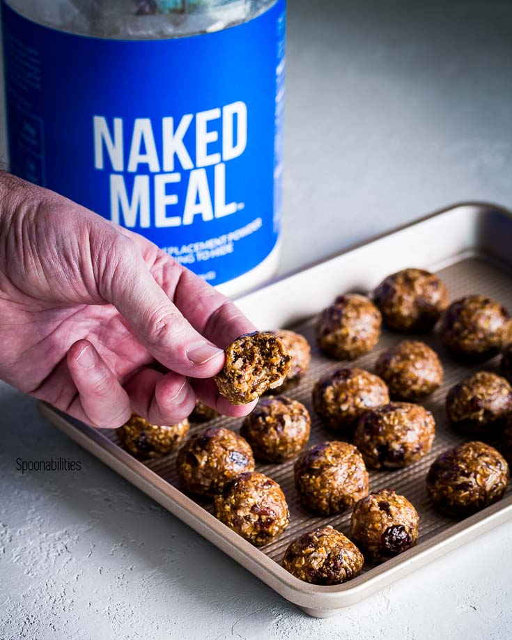 Hand holding a Protein Energy Bites and Naked Meal container in the background. Spoonabilities.com
