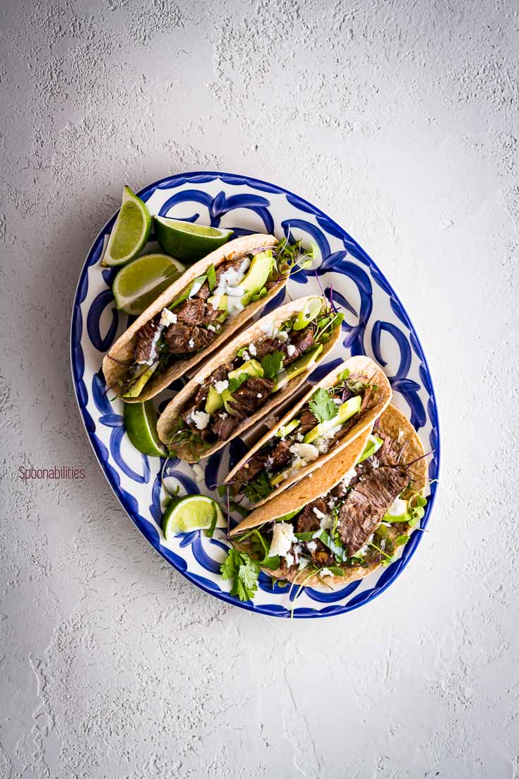 Oval serving plate in the center with four skirt steak tacos and garnish with lime. Spoonabilities.com