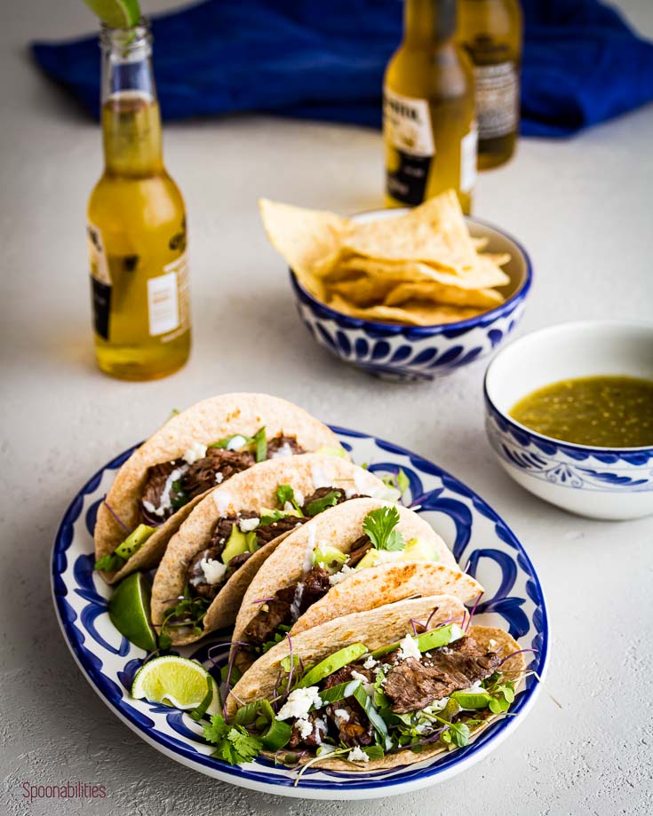 Oval serving plate with four Skirt steak tacos and three beers in the background. spoonabilities.com