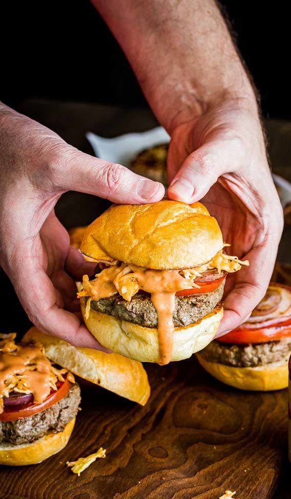 Two hands holding the burger with pink sauce dripping. 