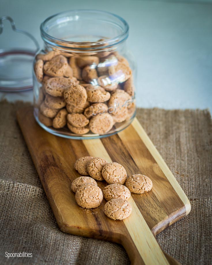 Amaretti cookies in a jar on top of a wooden board with some Amaretti cookies. Spoonabilities.com