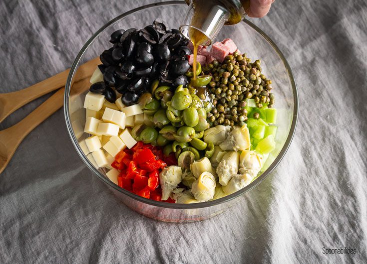 A large glass round mixing bowl with all the ingredients for the salad and pouring the dressing on it. Spoonabilities.com