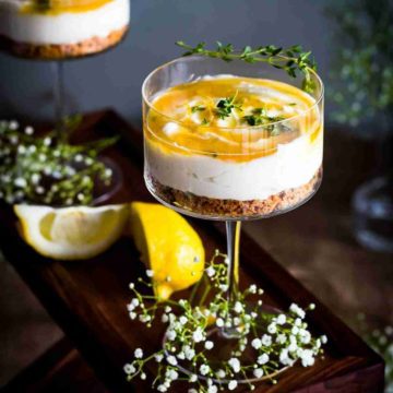 Honey Cheesecake in a cocktail glass with a hand drizzling the Honey-Thyme Drizzle. Spoonabilities.com