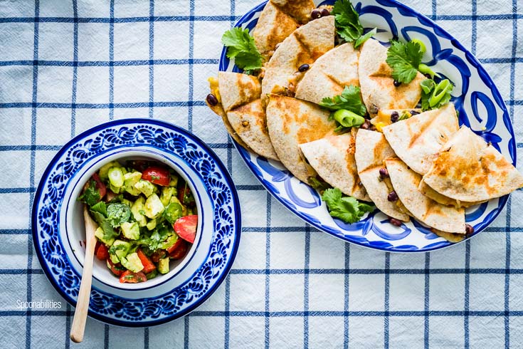 Overhead photo of the table setting with an oval serving plate in the top right side with Veggie Quesadillas and in the bottom left side a small round bowl with Cherry Tomato-Avocado Salsa. Spoonabilities.com