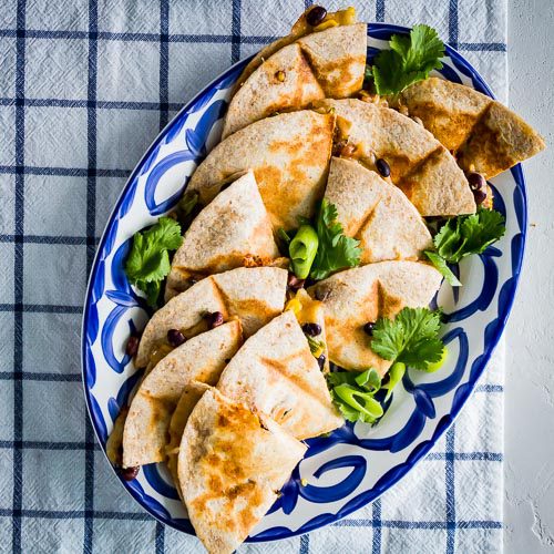 Veggie Quesadillas served in a blue & white oval serving plate on top of a white napkin with blue stripes. Spoonabilities.com
