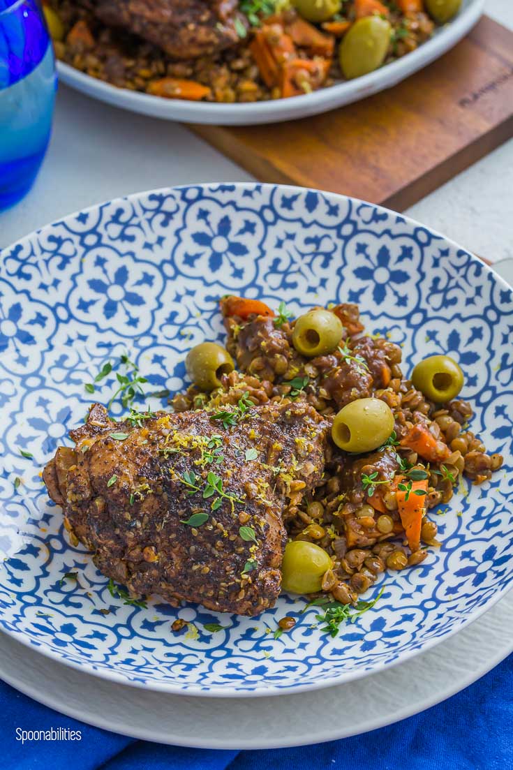 Blue and white bowl with braised Chicken thighs, lentils & carrots. Garnished with Green olives, lemon-thyme herbs & lemon zest. Spoonabilities.com