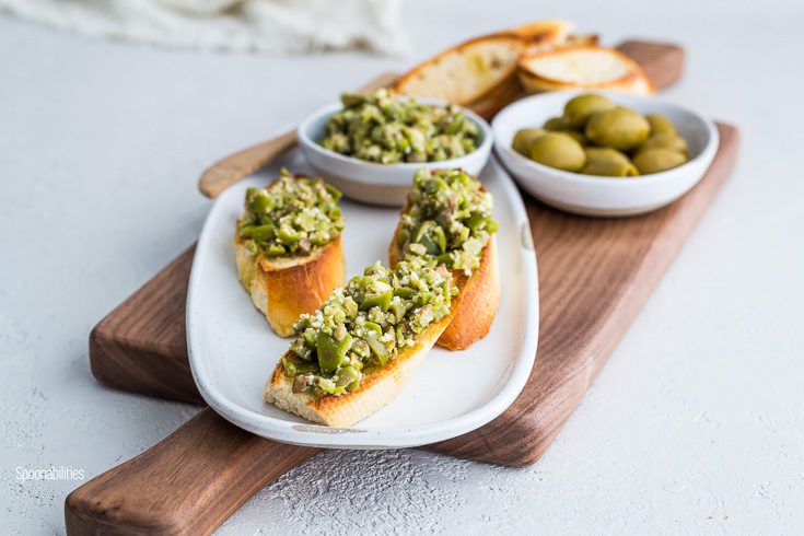 Narrow oval plate with three crostini with crushed green olives with Parmesan, garlic & olive oil. Spoonabilities.com