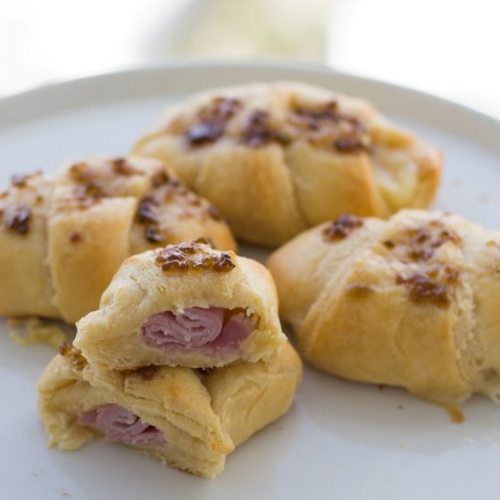 half cut ham and cheese crescent roll on plate with 3 other full rolls