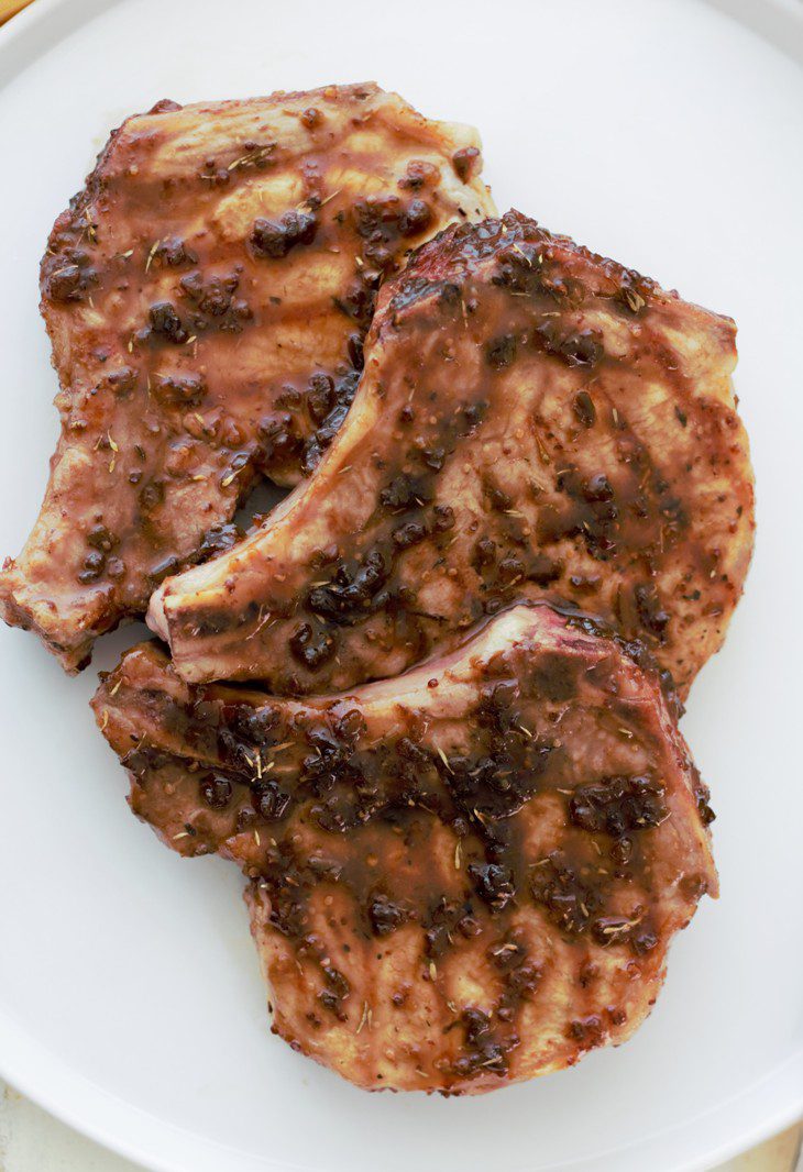 Closeup of three pork chops with raspberry jalapeno glaze on a white plate