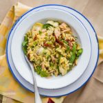 White pasta plate with blue rim with Mediterranean Orzo Salad is easy, light, and packed with flavorful ingredients like tuna, artichokes, sun-dried tomatoes, capers and a lemon Dijon Mustard Dressing