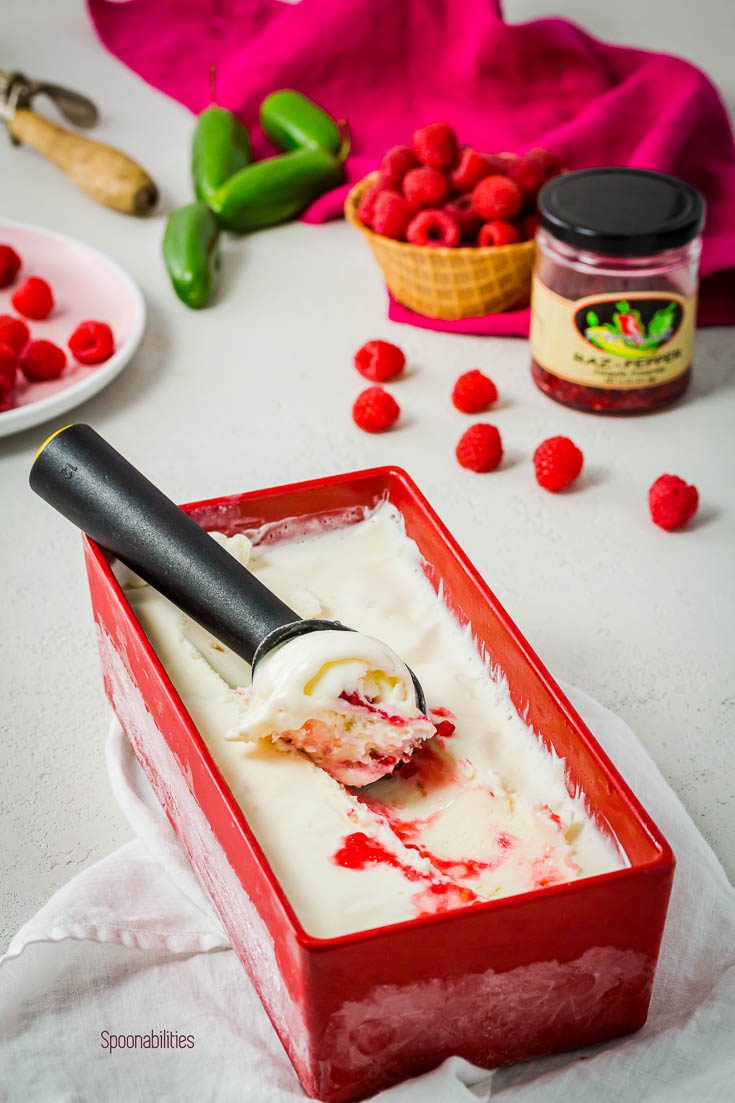 Homemade Raspberry Jalapeno ice cream in a red rectangular bowl on top of a white napkin. In the background a jar of Raspberry Jalapeño preserve. Available at Spoonabilities.com