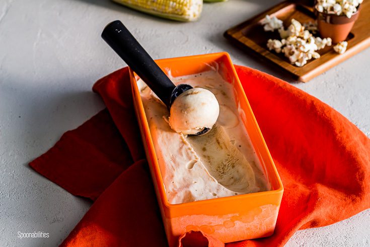 Caramel ice cream in a orange container on top of a orange napkin and popcorn in the background. Spoonabilities.com