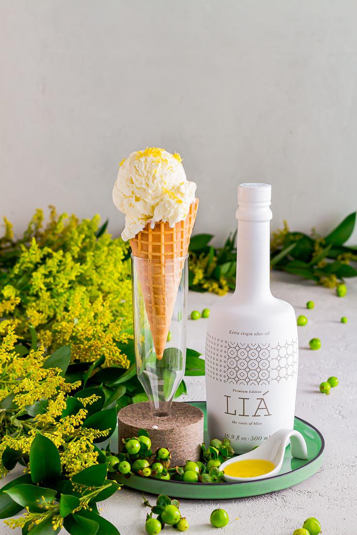 Ice cream in a waffle cone on a glass base with a felt support. The vase is on top of a green round plate and next is a white porcelain spoon with olive oil and a white bottle of LIA extra virgin olive oil. Available at Spoonabilities.com