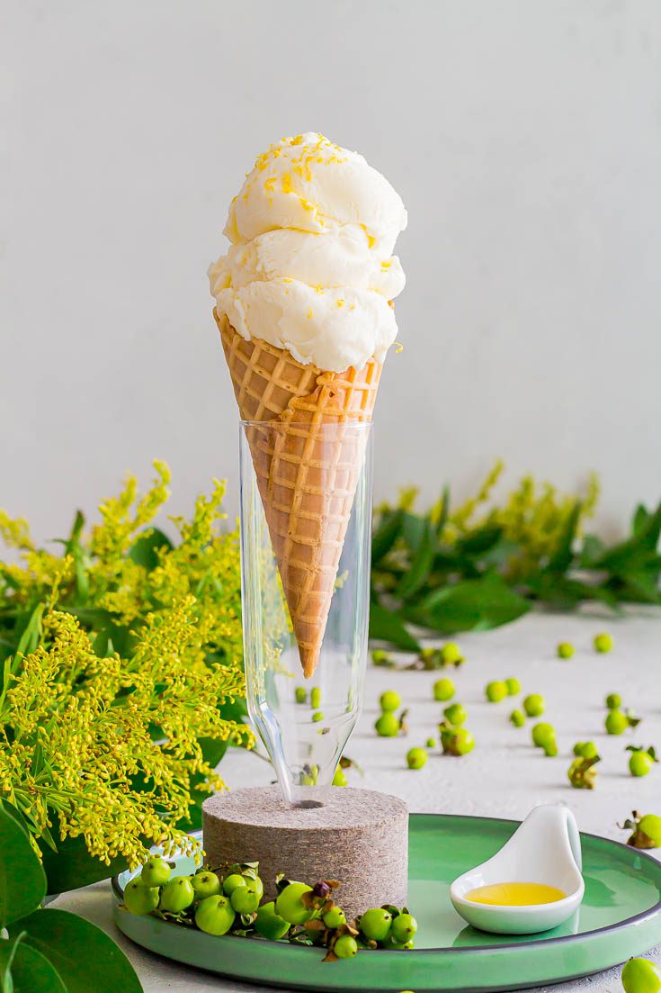 Ice cream in a waffle cone on a glass base with a felt support. The vase is on top of a green round plate and next is a white porcelain spoon with olive oil. Spoonabilities.com