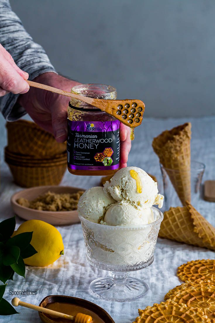 Three ice cream scoop in a glass bowl and a hand pouring Leatherwood Honey with a dipper. In the background waffle cones and Pizzelles. Spoonabilities.com