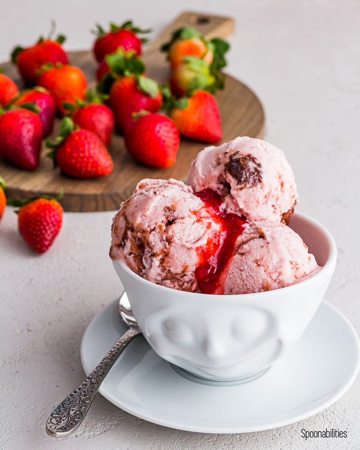 Smiling face bowl with strawberry ice cream with a spoon. In the background fresh strawberries. Spoonabilities.com