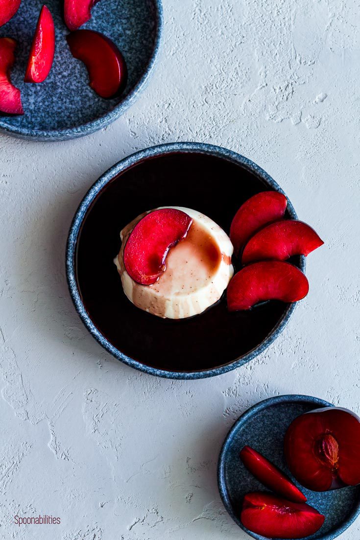 Three plates in a diagonal placement. In the center the panna cotta with red wine syrup and the two other plates with slices of plumcots. Spoonabilities.com