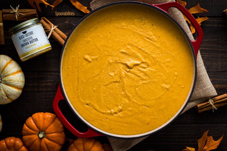 The Arepa in a red enameled cast iron casserole before go to the oven for 45 minutes. Next to the pot on the left side a jar of brown butter. The scene is decorated with Fall decor. Available at Spoonabilities.com