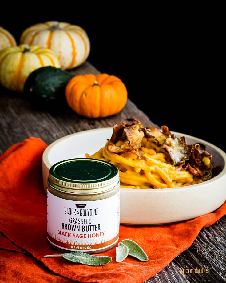 A jar of Grassfed brown butter with black sage honey in front of a pasta bowl. Spoonabilities.com